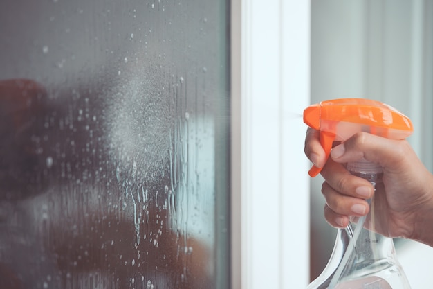 Woman hand cleaning window with cleanser spray