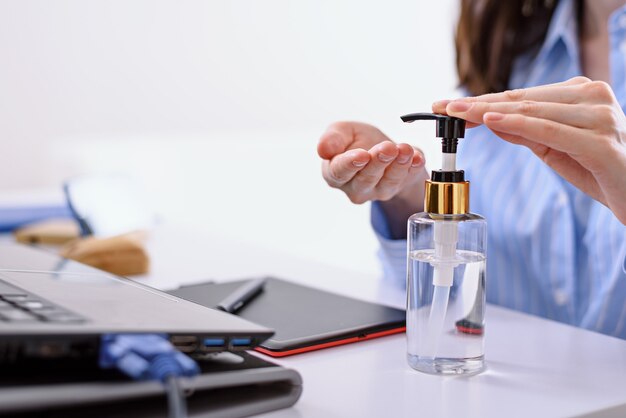 Woman hand cleaning with sanitizer, cleaning antibacterial gel for hands, remote work on laptop at home concept