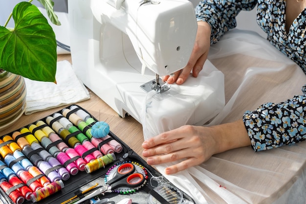 woman hand close up sews tulle on electric sewing machine filling the thread into the sewing needle adjusting the tension comfort in the house a housewife's hobby layout of sewing tools