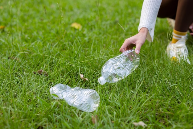 女性が草からプラスチックボトルを手で拾う