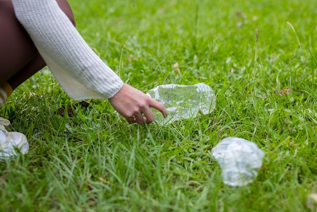 女性が草からプラスチックボトルを手で拾う