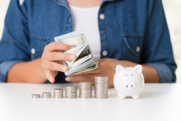 Woman hand counting America dollars banknotes money with stack of coins and piggy bank