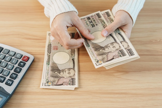 Woman hand counting Japanese Yen banknote with calculator Thousand Yen money Japan cash Tax Recession Economy Inflation Investment finance savings salary and payment concepts