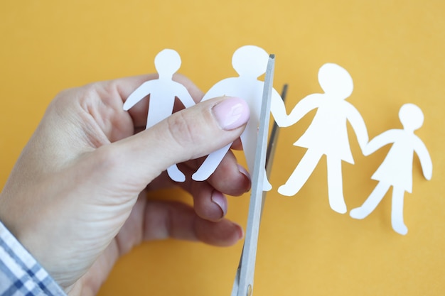 Woman hand cuts paper figures in form of family with scissors. Child and parents divorce concept