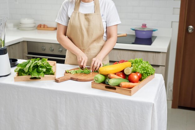 Woman hand cutting salad on chopping wood board with sharp\
knife and cooking vegetables salad in kitchen