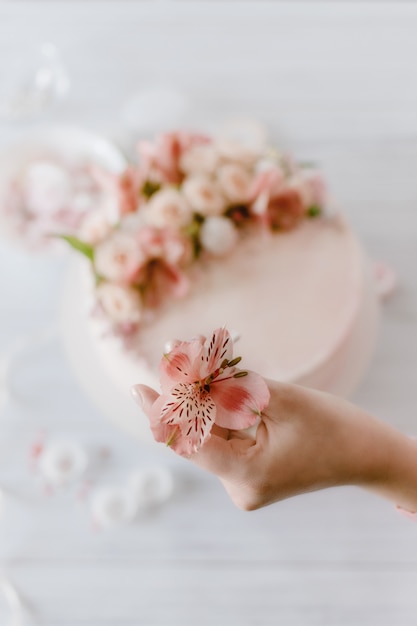 Рука женщины украшает розовый свадебный торт со свежими цветами.