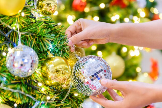 Woman hand decorating Christmas tree on bright bokeh background. 