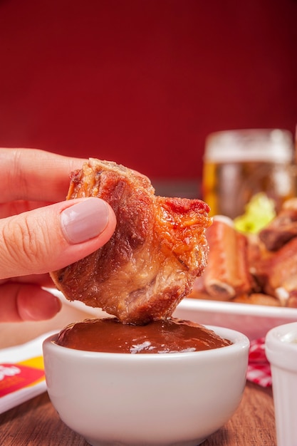 Woman hand dipping a fried pork rib in BBQ sauce