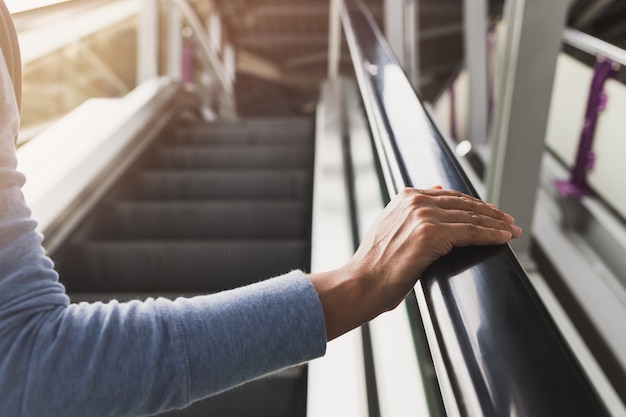 Mano della donna sul corrimano della scala mobile sulla stazione ferroviaria