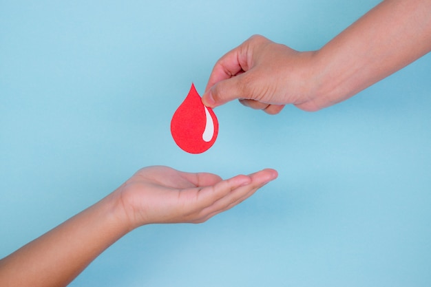 La mano della donna dà una goccia di sangue rosso ad una mano del ragazzo per il concetto di donazione di sangue, giornata mondiale del donatore di sangue.