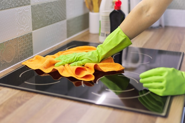 Foto mano della donna nei guanti che puliscono il piano cottura elettrico in ceramica della cucina, lucidando il vetro con un panno in microfibra