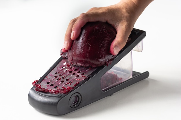 Woman hand grating cooked beetroot on grater for making salad on white background