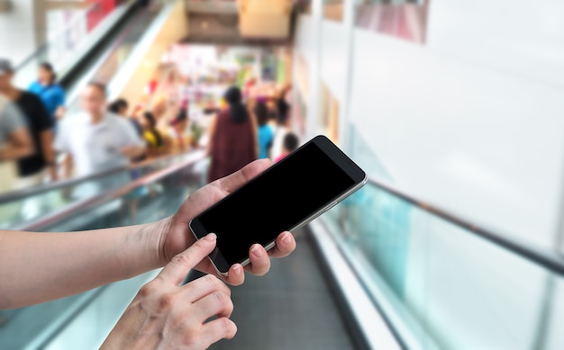 Фото Женщина держит руку и сенсорный экран смартфон на размытом движущемся эскалаторе с людьми
