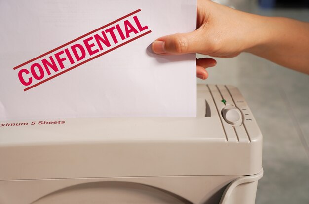 woman hand hold a confidential document with shredder machine