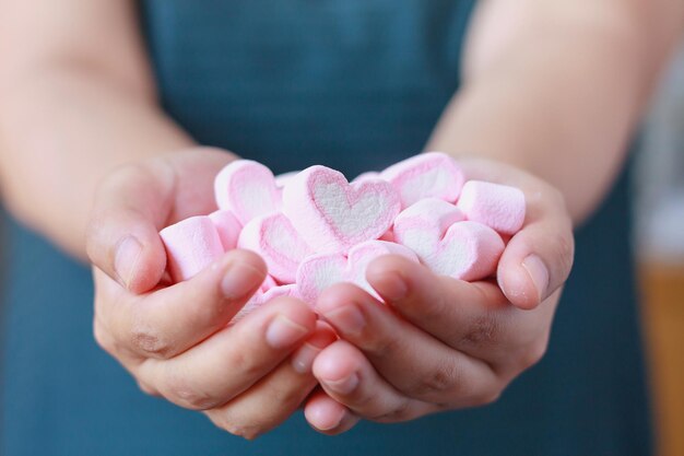 バレンタインデーのための女性の手はハート形のマシュマロを保持します