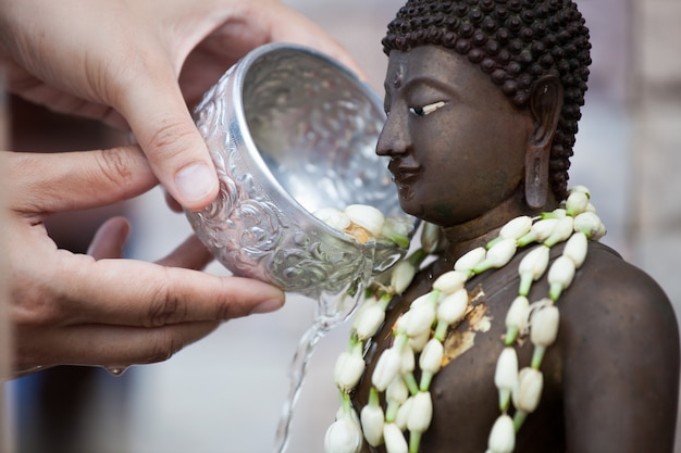 Woman hand hold little bowl to bath Buddha statue for blessing ceremony celebrate Songkran