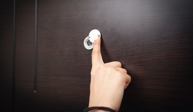 Woman hand hold peephole of wooden door.