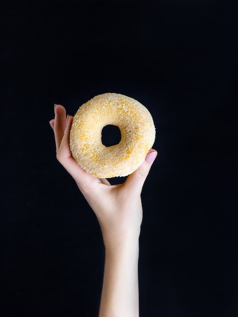 Woman hand hold sweet sugar donut on black background