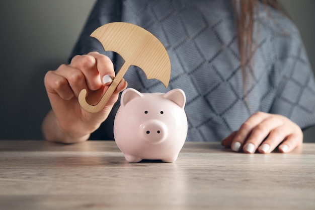 Woman hand hold the umbrella for protect to sick piggy bank