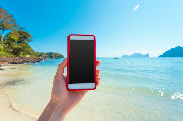 Woman hand hold white mobile phone with beautiful fresh sea and blue sky 