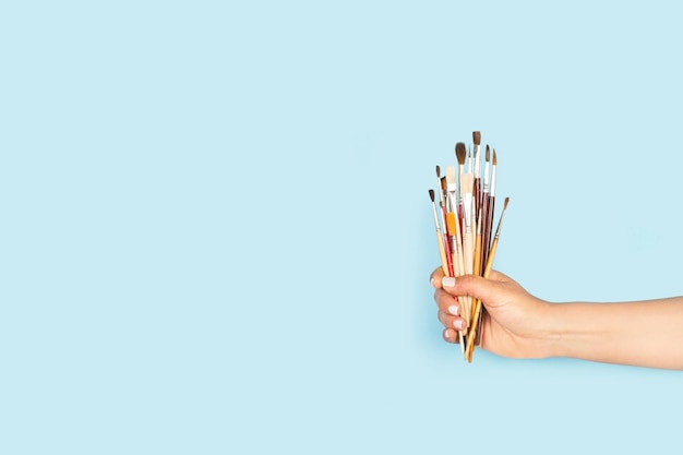 Woman hand holding artist paintbrushes on a light blue background with copy space