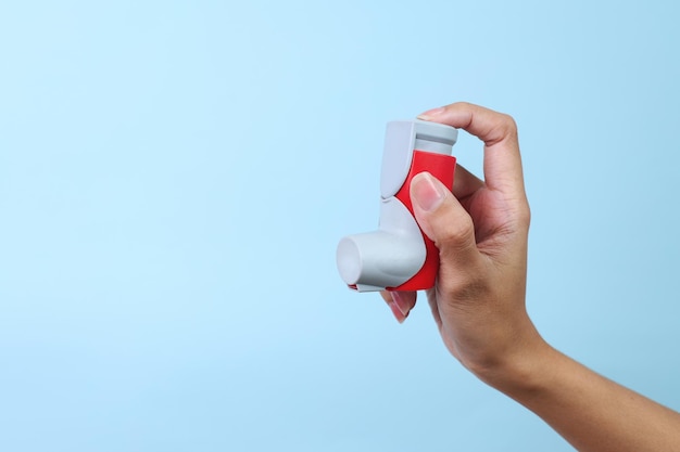 Photo woman hand holding asthma inhaler on blue background with space for text