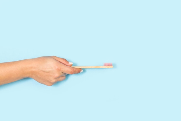 Woman hand holding bamboo toothbrush on a light blue background with copy space