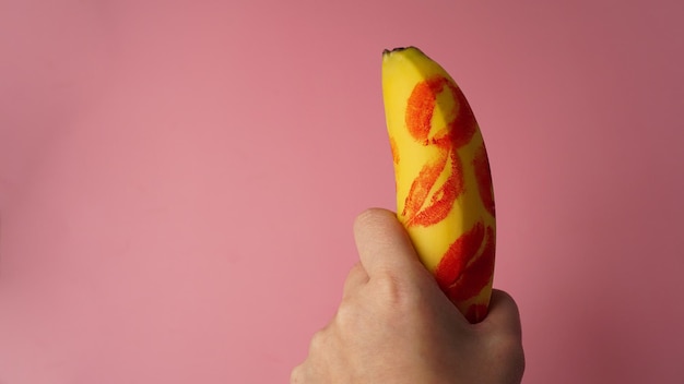 Mano della donna che tiene banana con segni di rossetto rosso su sfondo rosa