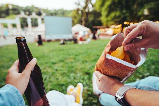 Woman hand holding beer bottle man hand holding chips open air cinema copy space