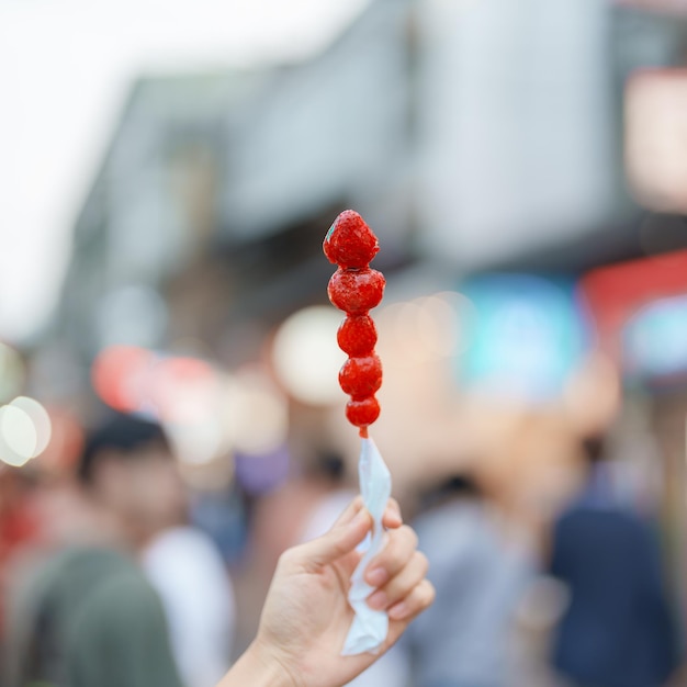 야시장 길거리 음식과 여행 컨셉에서 캐러멜 코팅 딸기 꼬치를 들고 있는 여성