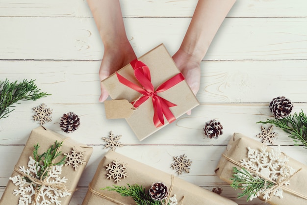 Contenitore di regalo dei regali di natale della tenuta della mano della donna su un fondo di legno della tavola