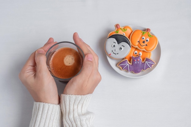 Mano della donna che tiene la tazza di caffè durante il consumo di divertenti biscotti di halloween felice giorno di halloween dolcetto o minaccia ciao ottobre autunno autunno festa tradizionale e concetto di vacanza