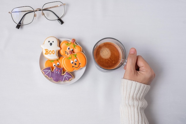 Woman hand holding coffee cup during eating funny halloween\
cookies happy halloween day trick or threat hello october fall\
autumn traditional party and holiday concept