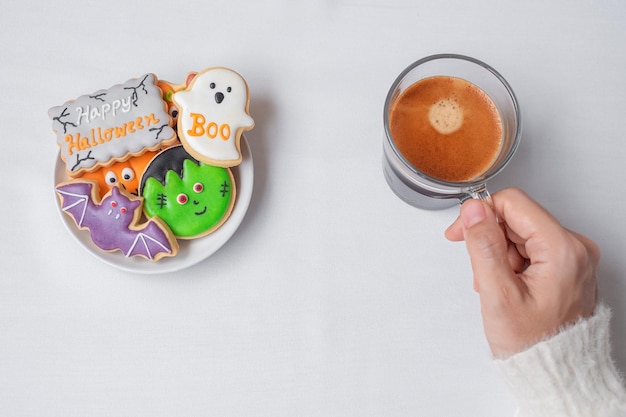 Woman hand holding coffee cup during eating funny Halloween Cookies Happy Halloween day Trick or Threat Hello October fall autumn Traditional party and holiday concept