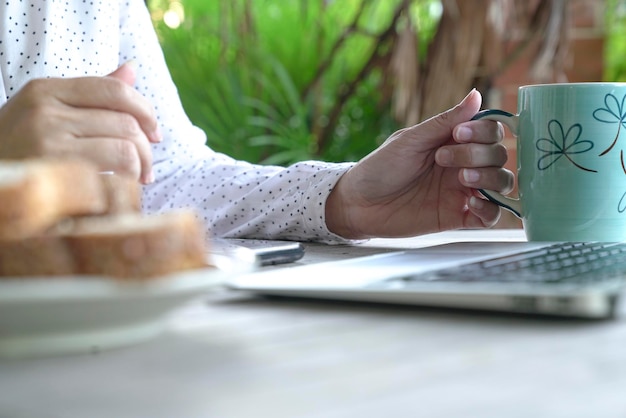Woman hand holding coffee cup in front of laptop