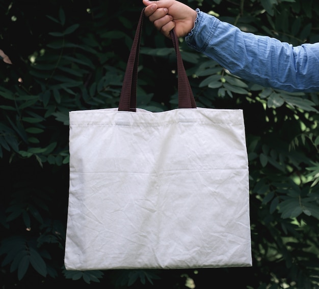 Woman of hand holding cotton Tote Bag on green leaf background. concept eco and recycling