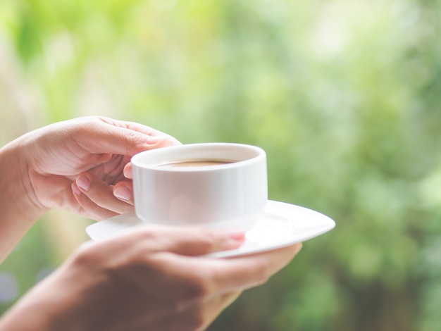 朝、庭でコーヒーを1杯持っている女性の手