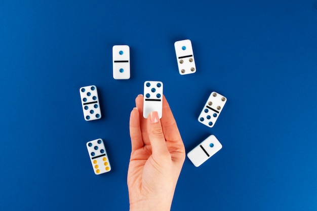 Mano della donna che tiene il pezzo di domino contro fondo blu, vista superiore