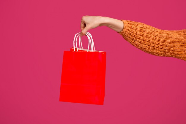 Woman hand holding empty red shopping bag over pink space