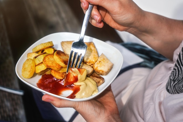 ジャガイモのグリルとフォークと皿、ケチャップとマスタードを添えた豆腐 (豆腐) - ベジタリアン バーベキュー/グリルを持っている女性の手