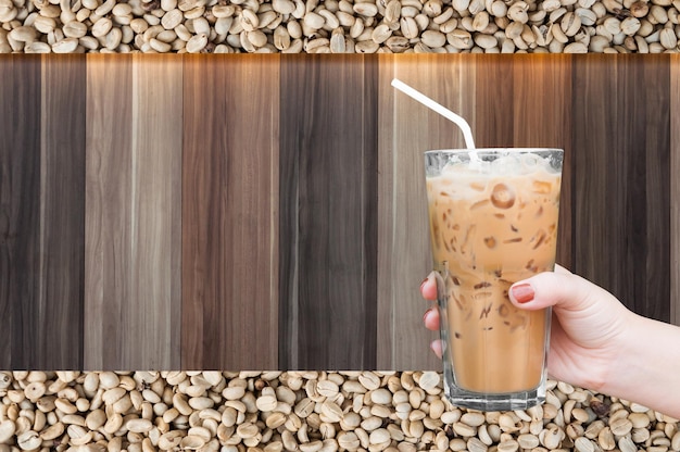 Woman hand holding the glass iced coffee on wooden and raw coffee beans backgroundIced latte coffee