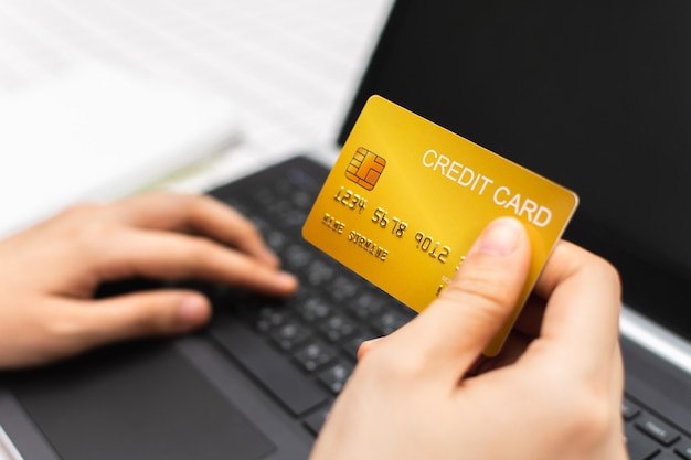 Woman hand holding gold credit card and using laptop computer Online shopping concept