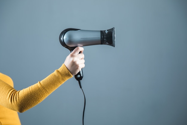 Woman hand holding hair dryer on grey background