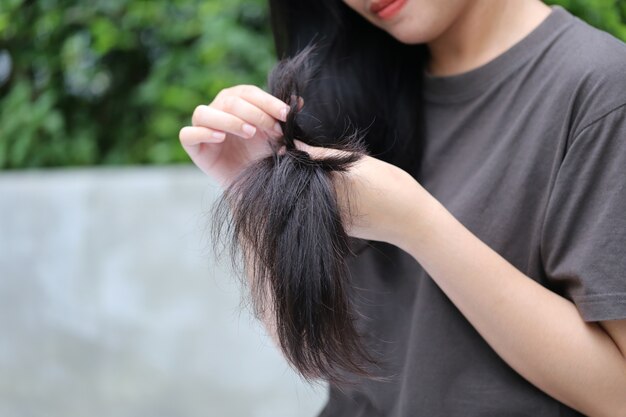 Woman hand holding her long hair with looking at damaged splitting ends of hair care problems