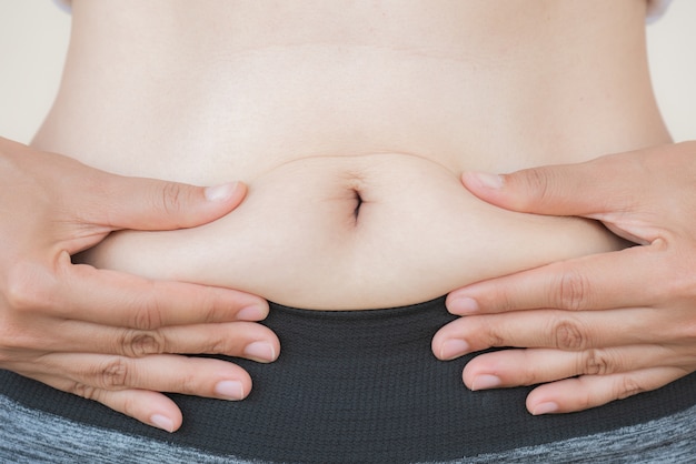 Woman hand holding her own belly fat.