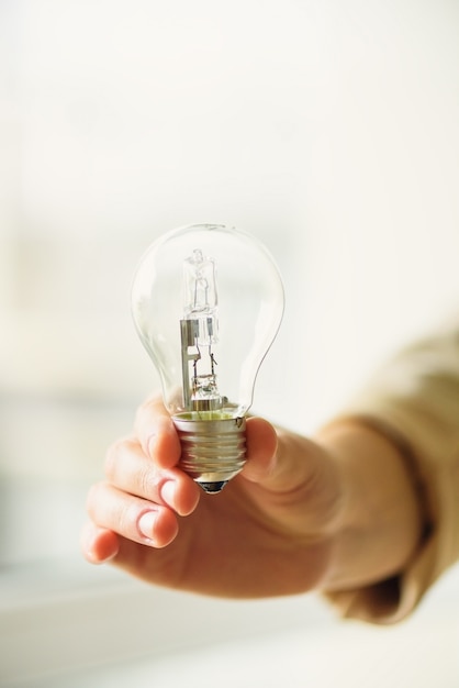 Woman hand holding light bulb on cream background with copy space. Creative idea, new business plan, motivation, innovation, inspiration concept.