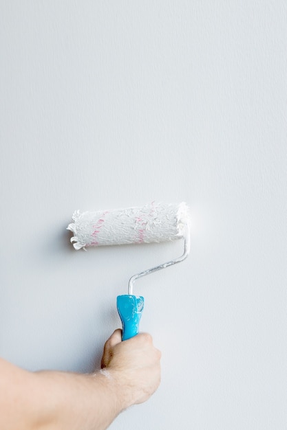 Woman hand holding a paint roller isolated on a white wall.