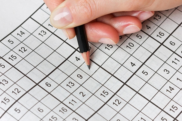 Foto la mano della donna che tiene una matita e risolve il popolare gioco di puzzle di sudoku con i numeri