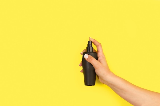 Woman hand holding a perfume sprayer on a yellow background with copy space