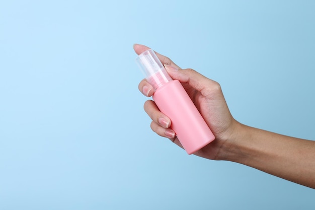 Woman hand holding pink blank small spray bottle mockup isolated on blue background